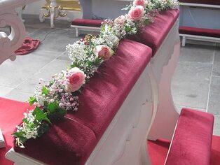 Kirchenbank mit einer Girlande aus rosafarbenen und weißen Blüten