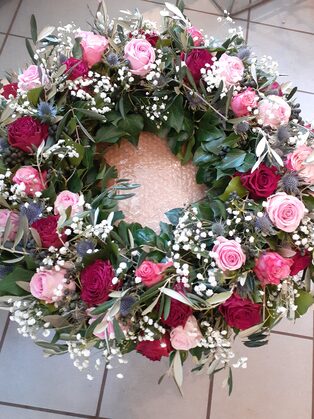 Trauerkranz aus rosafarbenen und roten Rosen mit Nelken