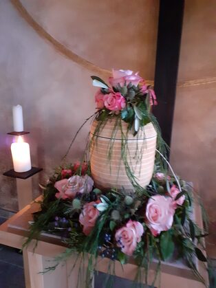 Urne mit Blumenschmuck aus rosafarbenen Rosen und einer Kerze