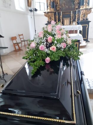 Dunkler Sarg mit einem Gesteck aus rosafarbenen Rosen in der Kirche