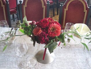 Tischgesteck aus roten Dahlien und Rosen auf weißer Tischdecke