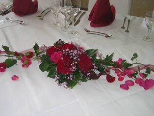 Tischläufer aus roten Rosen und Bougainvillea auf weißer Tafel