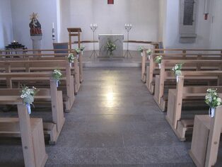 Mittelgang einer Kirche mit Blumenschmuck an den Bankreihen