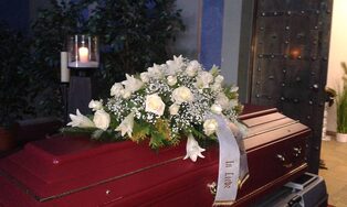 Roter Sarg mit einem Gesteck aus weißen Rosen und Lilien