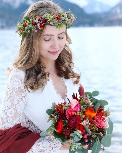 Braut mit Blumenkranz im Haar und einem Winterstrauß in Rot und Grün