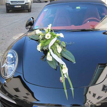 Autoschmuck aus weißen Callas und Bändern auf einem dunklen Sportwagen