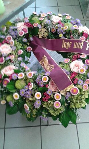 Trauerkranz aus hellen Blüten mit bordeauxroter Trauerschleife