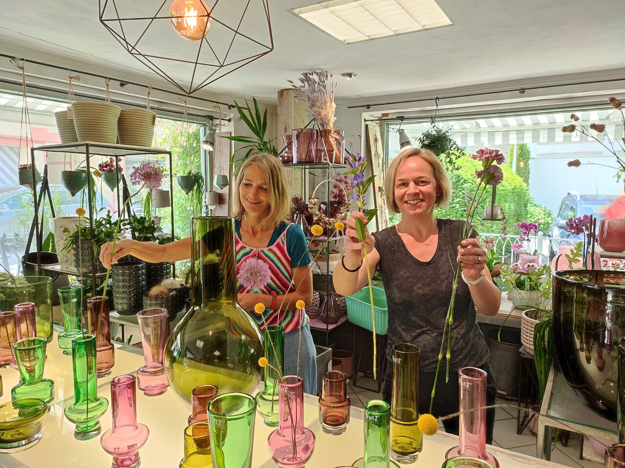Zwei Mitarbeiterinnen von Blumen Steber zwischen bunten Glasvasen im Laden