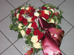 Herzförmiges Trauergesteck aus roten und weißen Rosen mit Schleife
