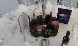 Festlich gedeckter Tisch mit dunklem Blumengesteck und Kerzen
