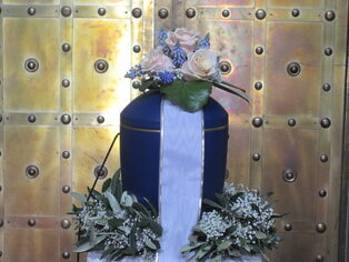 Blaue Urne mit weiß-blauem Blumenschmuck vor einer Kirchentür