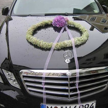 Kranz aus weißen Blüten mit Bändern auf einer dunklen Limousine