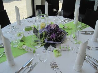 Runder Tisch mit grün-violettem Blumengesteck und Kerzen