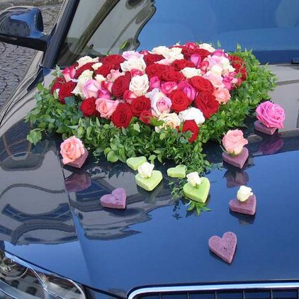 Autoschmuck aus roten und rosafarbenen Rosen mit Herzen auf blauer Haube