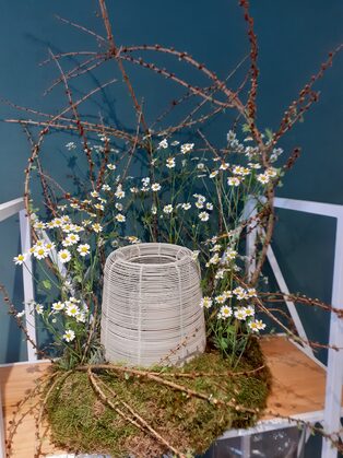 Urne aus Weidengeflecht mit Frühlingsblumen und Zweigen
